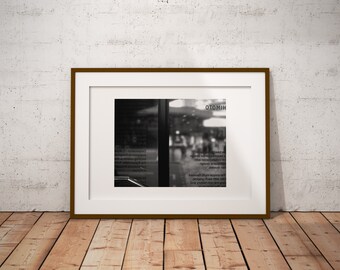 May include: A framed monochrome photograph of a shop front, with the word "OTOMIH" visible. The photograph is displayed on a wooden floor against a white brick wall. The shop front's glass reflects the interior and exterior.