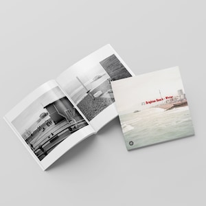 Può includere: Un libro di foto in bianco e nero con il titolo "Brighton Beach - Winter" sulla copertina. L'immagine della copertina mostra una vista della spiaggia con il mare in primo piano e la città sullo sfondo.