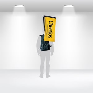 May include: A person wearing a black backpack with a yellow flag attached to it. The flag has the words "Cheerios cardboard rings" printed on it.
