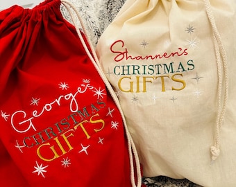 May include: Two personalized Christmas gift bags. One is red with white stars and the text "George's Christmas Gifts". The other is beige with silver stars and the text "Shannon's Christmas Gifts".