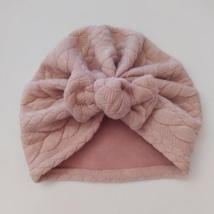 May include: A pink turban with a textured, woven design. The turban is tied in a knot at the top.