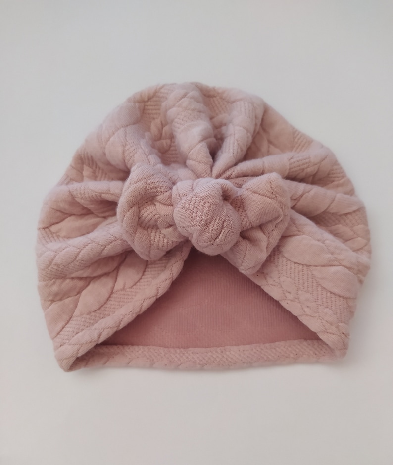May include: A pink turban with a textured, woven design. The turban is tied in a knot at the top.