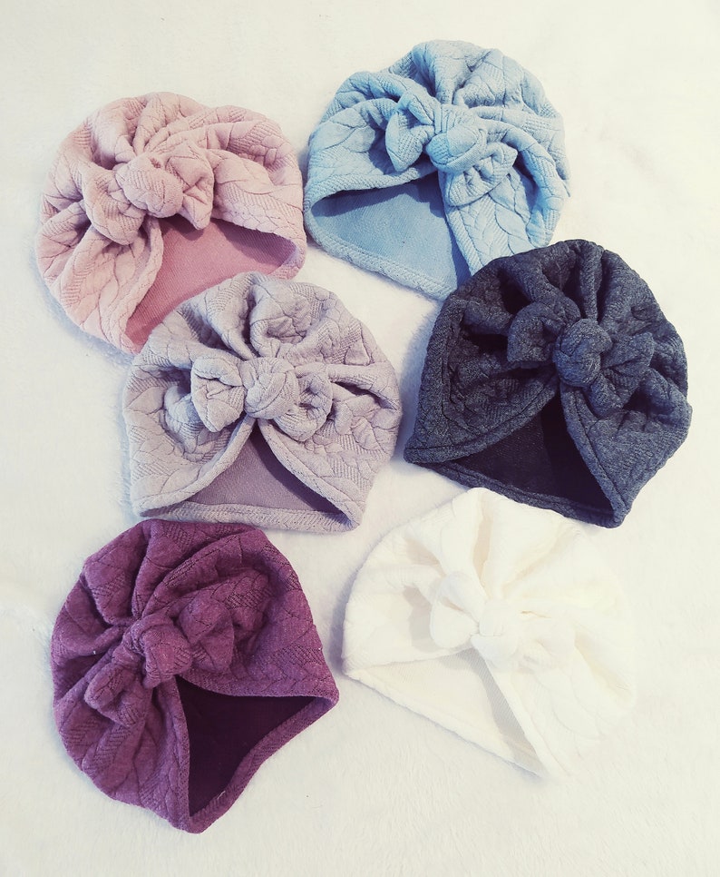 May include: Six different colored turban headbands with a knotted bow on top. The colors are light blue, pink, light gray, dark gray, white, and burgundy.