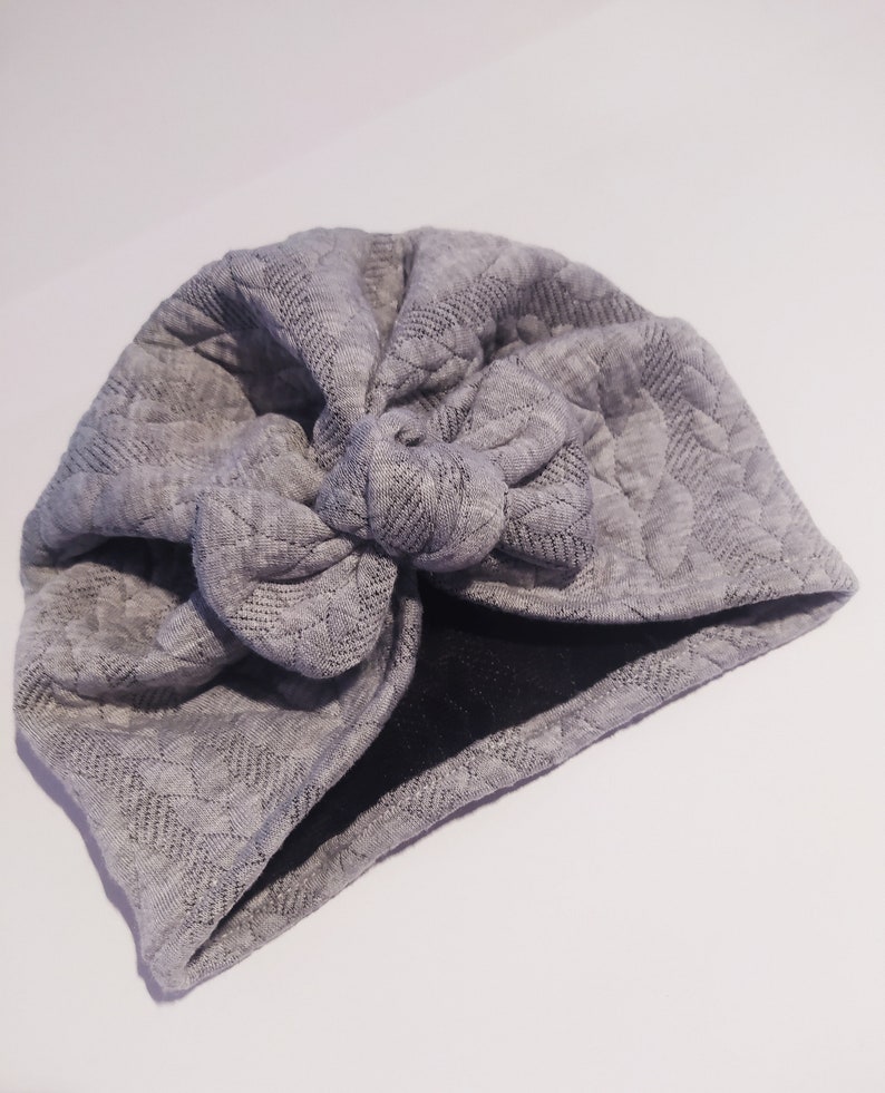 May include: Gray quilted turban with a knotted bow on top.