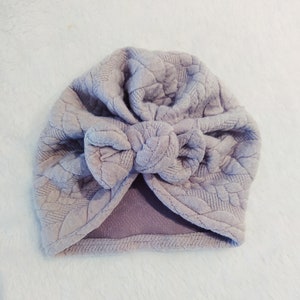 May include: A light purple turban with a textured fabric and a large bow on top.