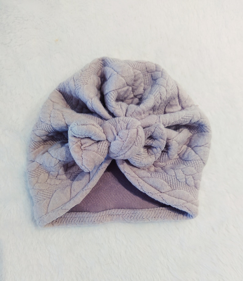 May include: A light purple turban with a textured fabric and a large bow on top.