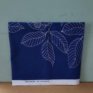 Puede incluir: Una tela azul con un patrón de hojas blancas. La tela tiene el texto "Design: Maria Astrom 2004 IKEA of Sweden AB" impreso en la parte inferior.