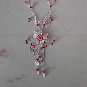 May include: A silver necklace with a red crystal flower pendant. The necklace has a delicate chain and a floral design with red crystals.