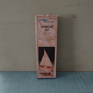 May include: A box for a sailboat model kit. The box is white with blue and red accents. The text on the box reads "Woodcrafter Kits ARIEL SERIES SAILBOAT KIT". The box shows a picture of a sailboat.