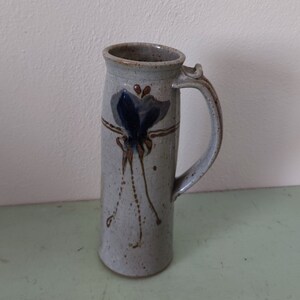May include: A ceramic mug with a brown, blue, and white butterfly design. The mug has a handle and is made in a rustic style.