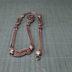 Peut inclure: Un collier en cha&icirc;ne argent&eacute;e avec un design d&eacute;coratif. La cha&icirc;ne a plusieurs brins et pr&eacute;sente des breloques orn&eacute;es en forme de paisley.