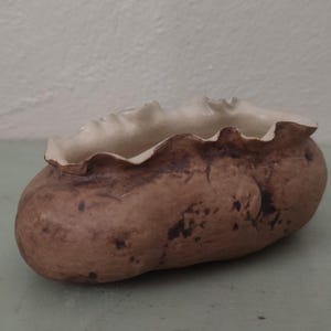 May include: A handcrafted, organic-shaped ceramic bowl. The exterior is a mottled brown with dark spots, while the rim is a ruffled, creamy white. This unique piece is ideal for serving or as a decorative accent.