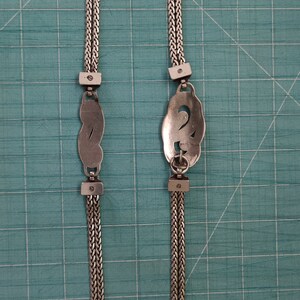 Peut inclure: Un collier en argent avec deux pendentifs d&eacute;coratifs. Les pendentifs sont en forme de huit et de lettre S stylis&eacute;e. La cha&icirc;ne est compos&eacute;e de deux brins d'argent.