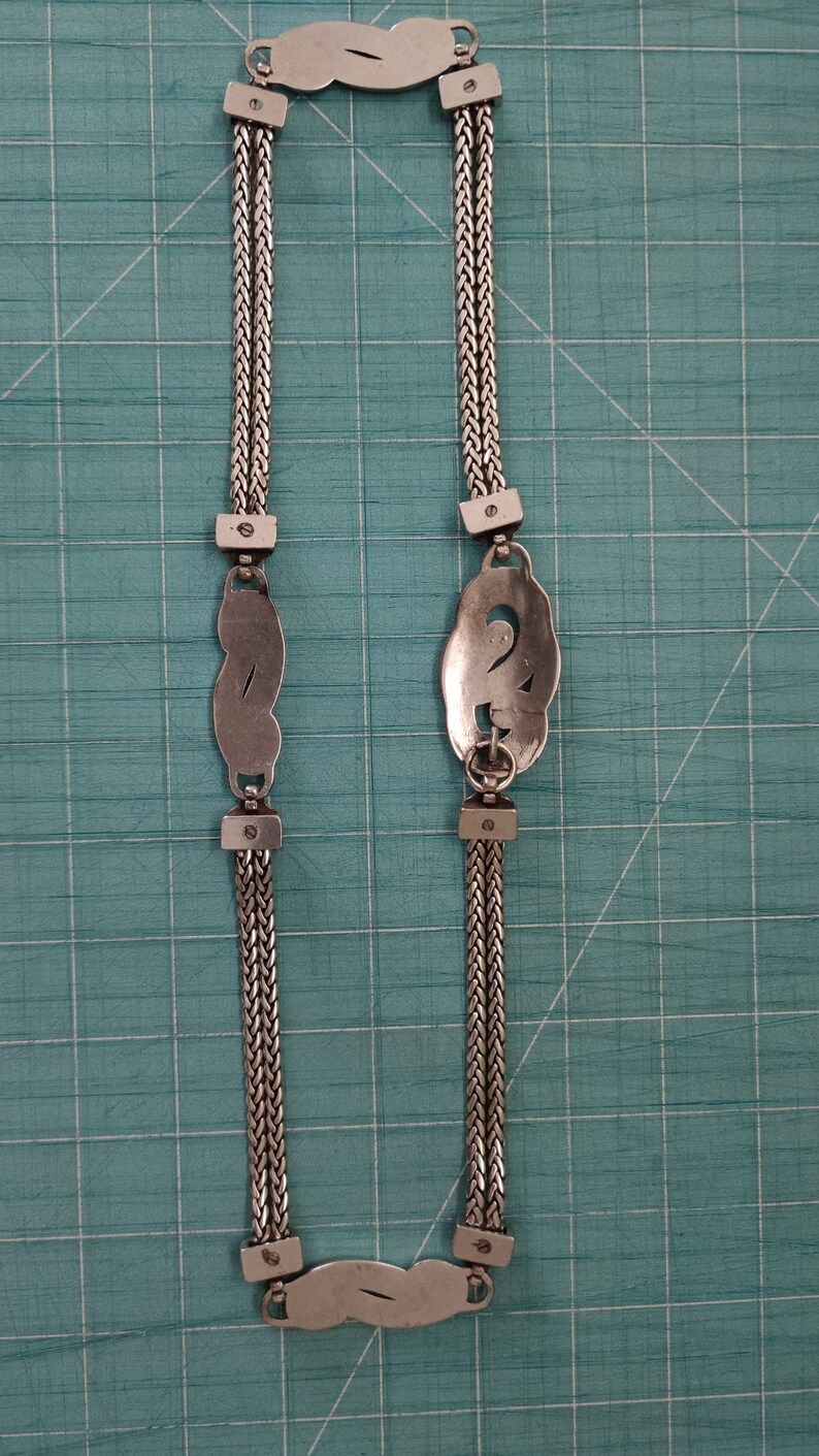 Peut inclure: Un collier en argent avec deux pendentifs d&eacute;coratifs. Les pendentifs sont en forme de huit et de lettre S stylis&eacute;e. La cha&icirc;ne est compos&eacute;e de deux brins d'argent.