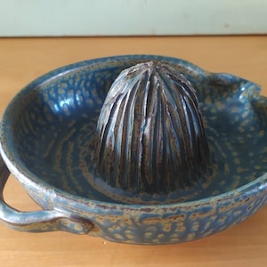 May include: A blue ceramic citrus juicer with a textured surface and two handles. The juicer has a cone-shaped reamer in the centre.