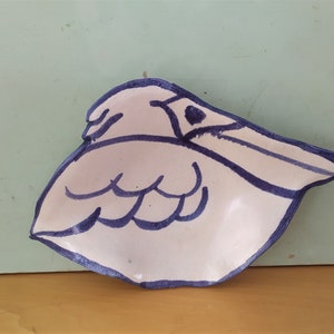 May include: A white ceramic dish shaped like a pelican with blue outlines. The dish has a textured surface and is perfect for serving small snacks or holding jewelry.