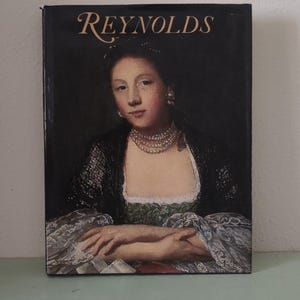 May include: A book cover featuring a portrait of a woman with a pearl necklace and a black shawl. The title "REYNOLDS" is printed in gold lettering at the top. The background is dark.