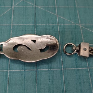 Peut inclure: Un bracelet en argent avec une cha&icirc;ne et un pendentif ovale d&eacute;coratif repr&eacute;sentant un chiffre "2" stylis&eacute;. Le bracelet se ferme avec un fermoir &agrave; ressort.