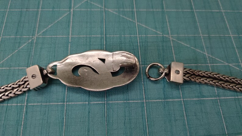 Peut inclure: Un bracelet en argent avec une cha&icirc;ne et un pendentif ovale d&eacute;coratif repr&eacute;sentant un chiffre "2" stylis&eacute;. Le bracelet se ferme avec un fermoir &agrave; ressort.