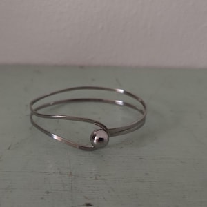 May include: A silver bangle bracelet with a single round bead accent.