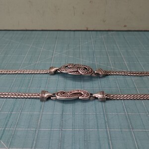 Peut inclure: Un collier en cha&icirc;ne argent avec deux fermoirs d&eacute;coratifs orn&eacute;s d'argent. La cha&icirc;ne est compos&eacute;e de deux brins de maillons d'argent.