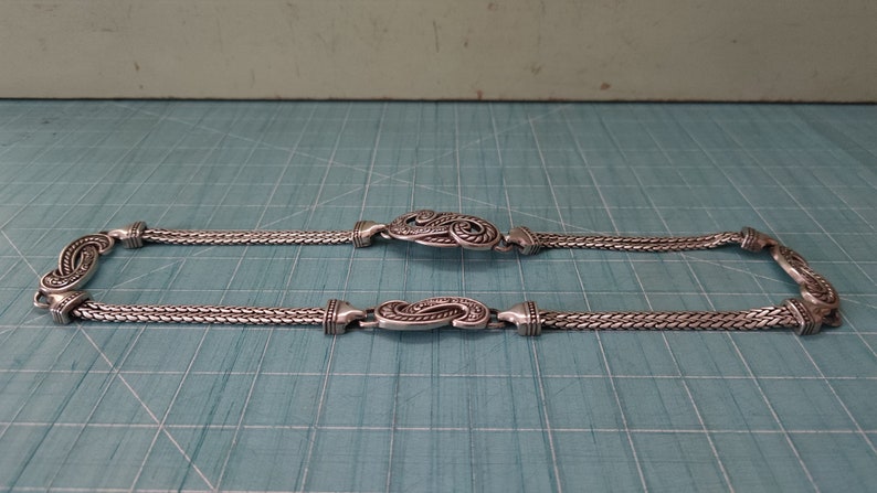 Peut inclure: Un collier en cha&icirc;ne argent avec deux fermoirs d&eacute;coratifs orn&eacute;s d'argent. La cha&icirc;ne est compos&eacute;e de deux brins de maillons d'argent.