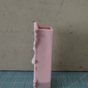 Puede incluir: Un jarr&oacute;n de cer&aacute;mica rosa claro con un dise&ntilde;o decorativo y ornamentado. El jarr&oacute;n es alto y estrecho, con forma rectangular.