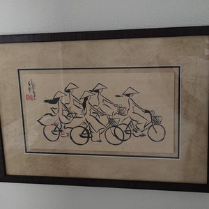 May include: Black and white ink drawing of five women wearing conical hats riding bicycles. The drawing is framed in a dark wood frame.