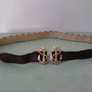 Puede incluir: Un cinturón tejido de colores con una hebilla de cuero marrón con dos cierres en forma de ancla de oro.