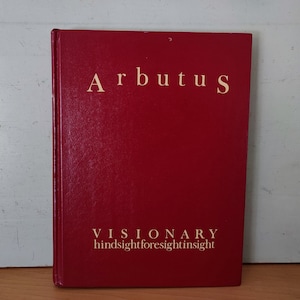 May include: A hardcover book titled "Arbutus" in a deep red color. The title and the word "VISIONARY" are in gold lettering. Below "VISIONARY" are the words "hindsightforesightinsight".