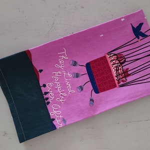 May include: Pink tea towel with a hot air balloon illustration and the text "They lived happily ever after".