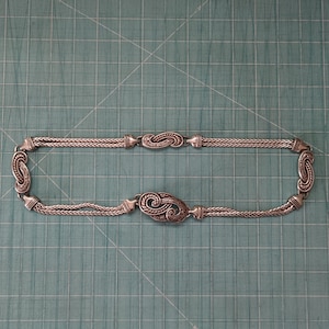 Peut inclure: Un collier en cha&icirc;ne argent avec un pendentif d&eacute;coratif et orn&eacute;. Le pendentif a la forme d'un tourbillon ou d'une vague.