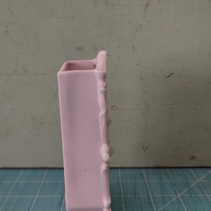 Puede incluir: Un jarr&oacute;n de cer&aacute;mica rosa p&aacute;lido con un dise&ntilde;o decorativo en el lateral. El jarr&oacute;n est&aacute; sobre una superficie de rejilla azul y blanca.