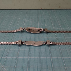 Peut inclure: Un collier en cha&icirc;ne argent avec deux pendentifs de forme ovale. Chaque pendentif pr&eacute;sente un motif stylis&eacute; et est reli&eacute; &agrave; la cha&icirc;ne par un petit anneau en argent.