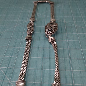 Peut inclure: Un collier en cha&icirc;ne argent avec un pendentif d&eacute;coratif en forme de paisley. Le pendentif est d&eacute;taill&eacute; avec des volutes et des lignes complexes.