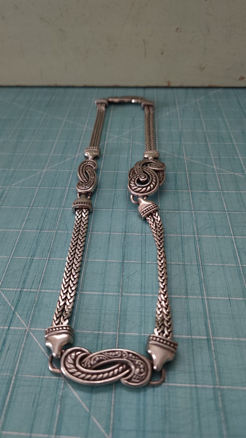 Peut inclure: Un collier en cha&icirc;ne argent avec un pendentif d&eacute;coratif en forme de paisley. Le pendentif est d&eacute;taill&eacute; avec des volutes et des lignes complexes.