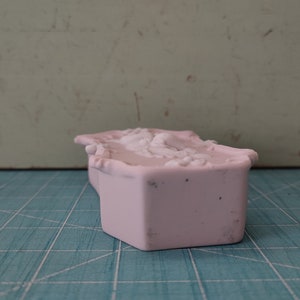 Puede incluir: Una caja de cer&aacute;mica rosa con un dise&ntilde;o floral decorativo. La caja est&aacute; cerrada y tiene una forma rectangular.