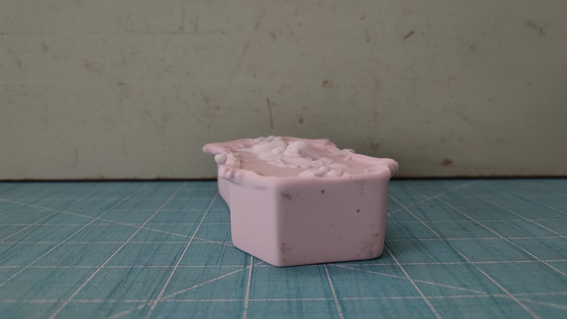 Puede incluir: Una caja de cer&aacute;mica rosa con un dise&ntilde;o floral decorativo. La caja est&aacute; cerrada y tiene una forma rectangular.