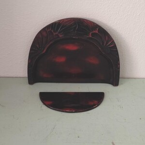 May include: A two-piece, dark red, decorative tray set. The larger piece is semi-circular with a floral carved border. The smaller piece is a matching semi-circle. The set is on a light green surface.