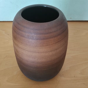 Könnte beinhalten: Eine braune Keramikvase mit dunkelbrauner Glasur und einer breiten Öffnung. Die Vase hat eine glatte, abgerundete Form.