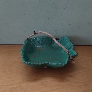 Puede incluir: Un plato de cerámica de color verde azulado con un asa de rama blanca. El plato tiene un borde festoneado y un diseño floral.