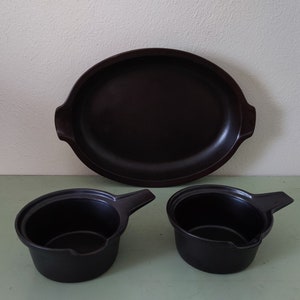May include: A set of three black ceramic cookware pieces, including a large oval baking dish and two smaller round saucepans with handles.