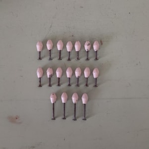 May include: A collection of small, light pink objects with dark brown stems, arranged in three rows on a light green surface. The objects have a rounded, elongated shape, resembling miniature light fixtures or decorative elements.