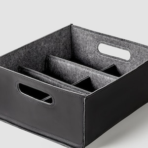 May include: Black leather storage box with a gray felt interior divided into three compartments. The box has two cut-out handles on the sides.