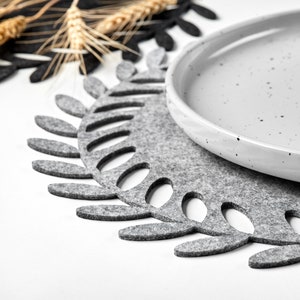 Può includere: Un sottopentola in feltro grigio con un design a foglia e un piatto in ceramica grigia macchiata sopra.