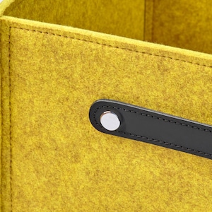 May include: A yellow felt storage box with a black leather handle and a silver metal button.