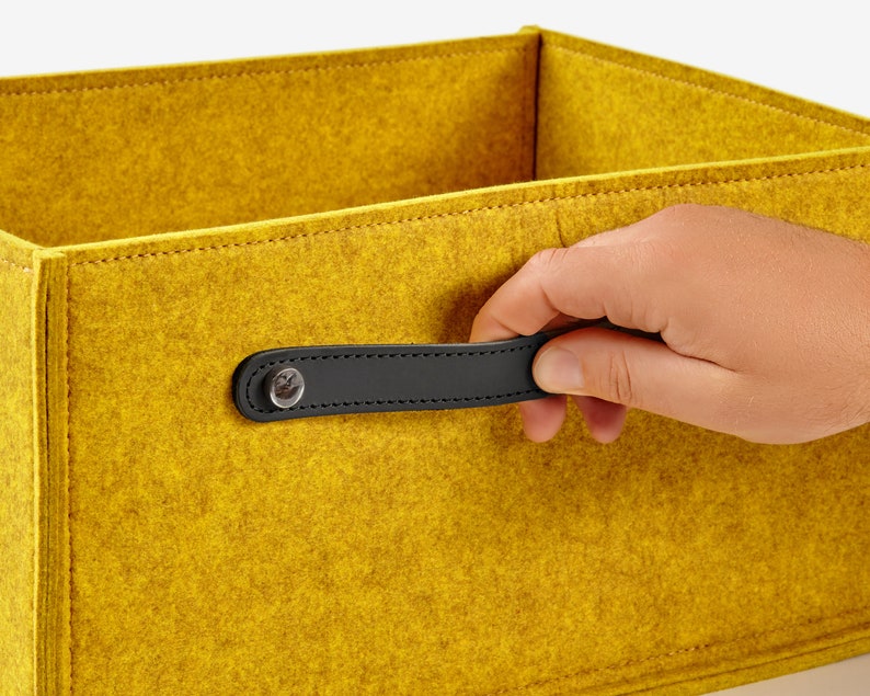 May include: A yellow felt storage box with a black leather handle. The handle has a small metal button.