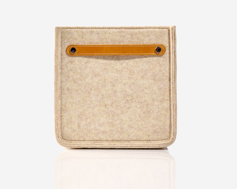May include: A beige felt storage box with a brown leather handle and two metal rivets. The box has a stitched edge.