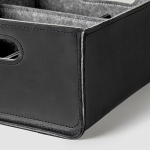 May include: Black leather storage box with a gray felt interior and multiple compartments. The box has a stitched edge and a handle.