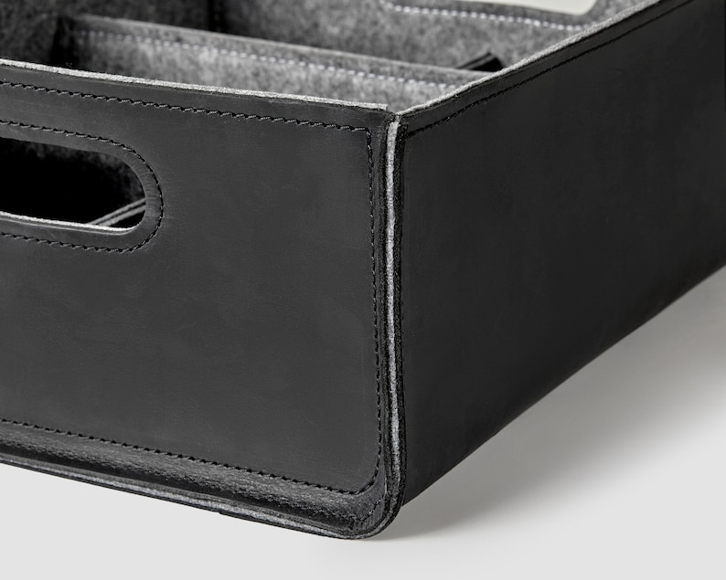 May include: Black leather storage box with a gray felt interior and multiple compartments. The box has a stitched edge and a handle.